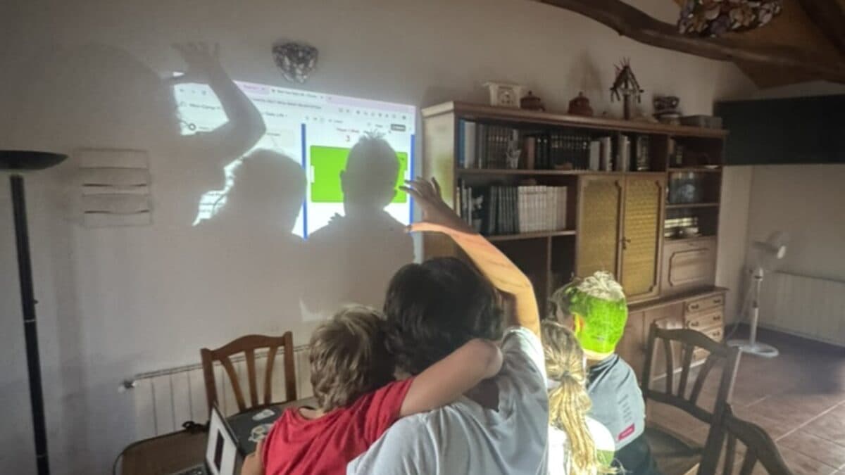 Kids huddled together watching a game they built, projected on the wall at the original camp in León