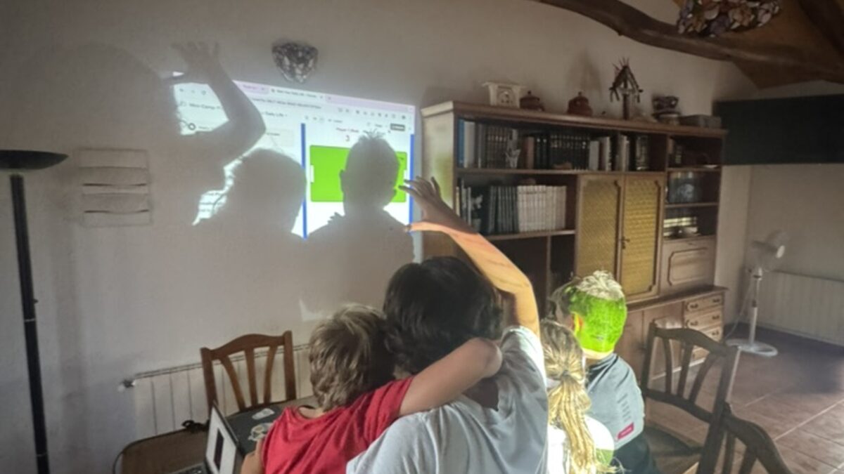 Niños abrazados viendo un juego que construyeron, proyectado en la pared del campamento original en León
