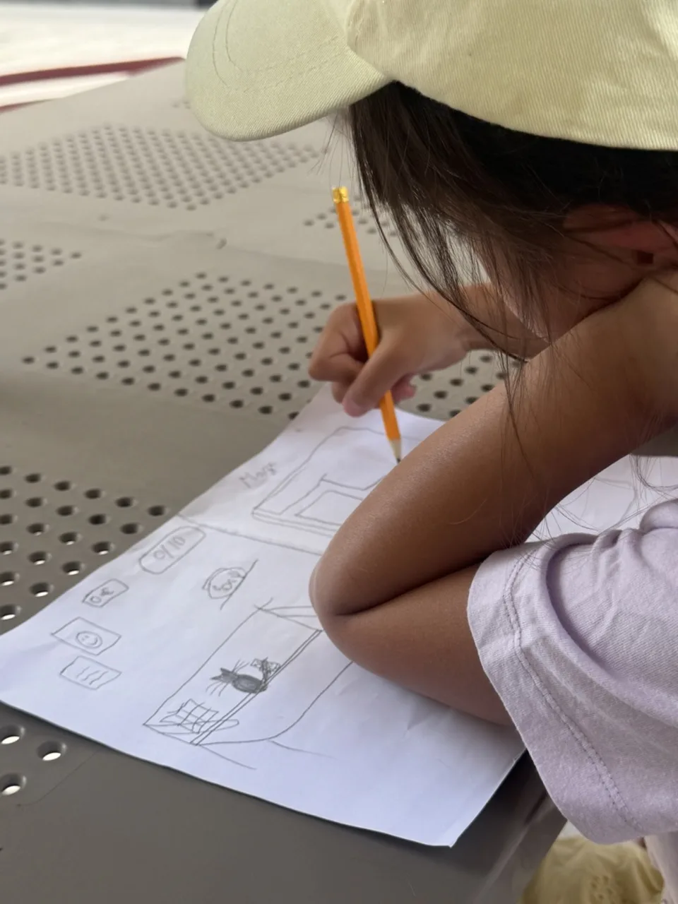 A child in a cap drawing a game plan in pencil at an outdoor table